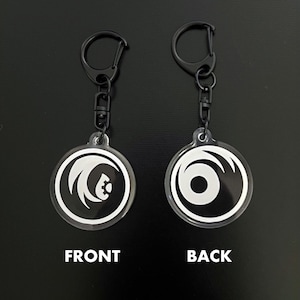 May include: Two clear acrylic keychains with black hardware. Each keychain has a circular design with a white graphic. One side is labeled "FRONT" and the other "BACK". The front design features a stylized emblem, while the back has a simple circular design.