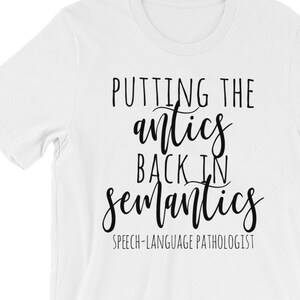 May include: White t-shirt with black text that reads "Putting the antics back in semantics" and "Speech-Language Pathologist".