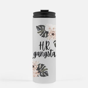 May include: A white travel mug with a black lid features the text "HR gangsta" in black script. Floral designs with pink and white flowers and green leaves are placed above and below the text.