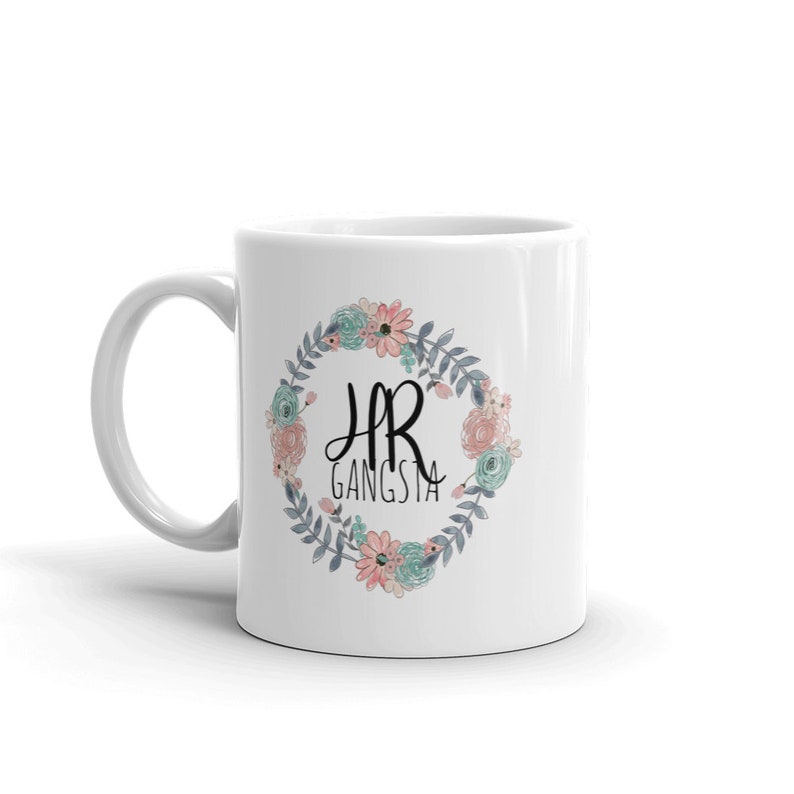May include: White ceramic mug with a floral wreath design. The wreath is in shades of blue, pink, and green. The text "HR Gangsta" is in the center of the wreath.
