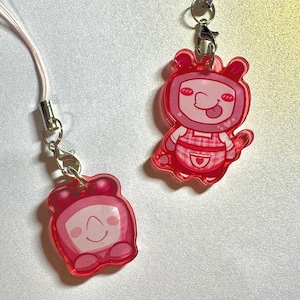 May include: Two pink acrylic charms with silver-tone hardware. One charm is a smiling alarm clock, and the other is a character with a tongue sticking out, wearing an apron. Both charms are attached to a lanyard.
