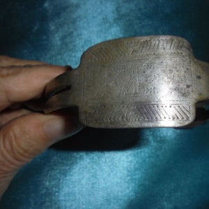 May include: A silver metal bracelet with an engraved design and the word "SOUVENIR" on the top.