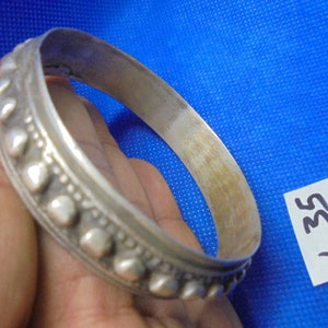 May include: A silver bangle bracelet with a decorative design of small, raised circles and a smooth, polished finish.