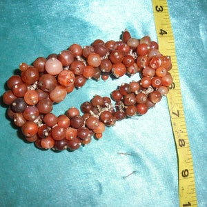 Könnte beinhalten: Eine Kette aus Karneolperlen, die mit Silberdraht aufgereiht sind, in Herzform. Die Perlen sind in einem Mix aus Rot, Orange und Braun.