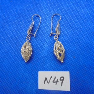 May include: A pair of silver dangle earrings with a delicate, intricate design. The earrings are in the shape of a teardrop and have a small loop at the top for attaching to an earring hook. The earrings are labeled with the number "N49".
