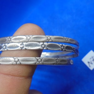 May include: Three silver bangles with an intricate design of oval shapes and small dots. The bangles are stacked on top of each other.