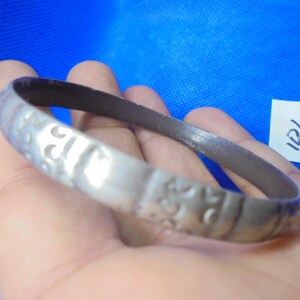 May include: A silver bracelet with an intricate design. The bracelet is made of metal and has a smooth finish.