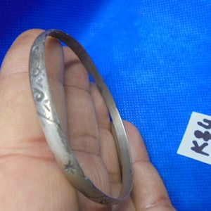 Puede incluir: Un brazalete de plata con un diseño intrincado. El brazalete está grabado con un patrón de estrellas y otros símbolos.