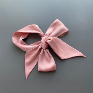May include: A pink satin ribbon tied into a bow. The ribbon is soft and silky.