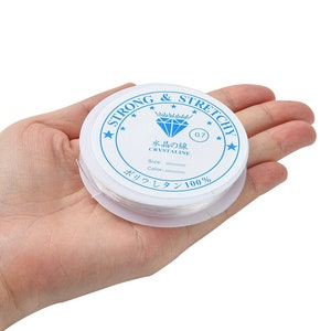 May include: A white spool of strong and stretchy elastic string for jewelry making. The label reads "Strong & Stretchy", "Crystaline", "0.7", "Size:", "Color:", "Polyurethane 100%".