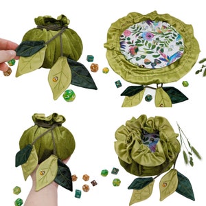 Puede incluir: Cuatro bolsas de dados de terciopelo verde con adornos de hojas y una bandeja de dados de sat&eacute;n verde con estampado floral. Las bolsas de dados est&aacute;n llenas de dados de colores.