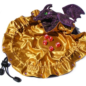 May include: A gold satin dice bag with a purple dragon design and red dice inside. The bag has a drawstring closure and a black cord.