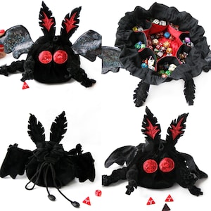 May include: Black plush dice bag shaped like a moth, with red accents on the eyes and antennae. The bag has iridescent wings and a drawstring closure. Several dice are visible inside the open bag, and small red dice are scattered around.