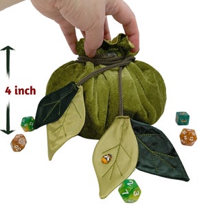 Puede incluir: Bolsa de dados de terciopelo verde con cierre de cord&oacute;n y detalles de hojas. La bolsa mide 18 cm de ancho y 10 cm de alto. La bolsa se muestra con dados.