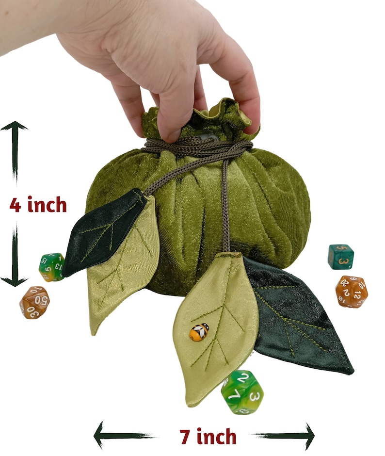 Puede incluir: Bolsa de dados de terciopelo verde con cierre de cord&oacute;n y detalles de hojas. La bolsa mide 18 cm de ancho y 10 cm de alto. La bolsa se muestra con dados.
