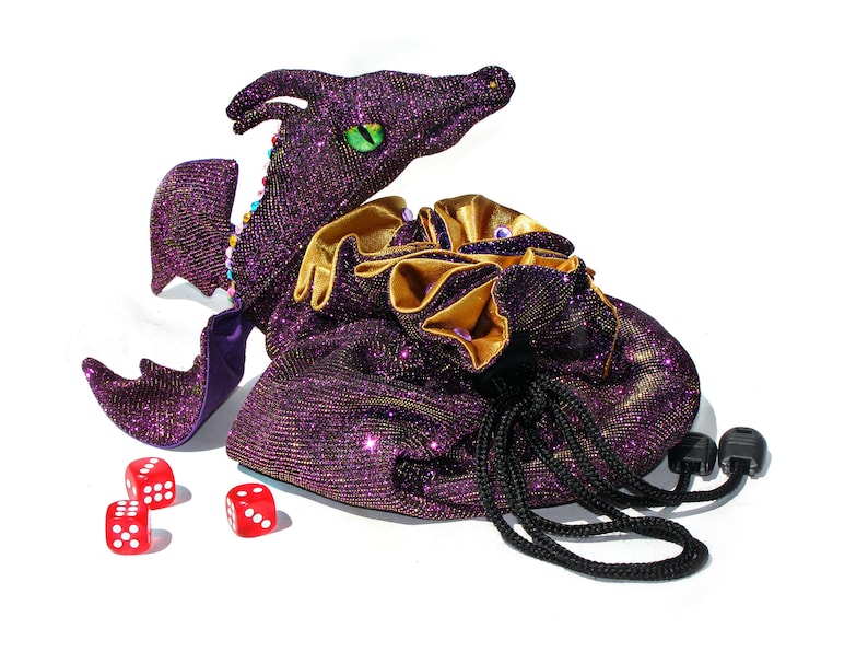 May include: A purple and gold sparkly dragon-shaped dice bag with a drawstring closure and black cords. Three red dice are scattered in front of the bag.