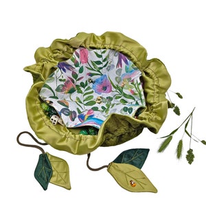 Puede incluir: Una bolsa de dados de terciopelo verde con cierre de cord&oacute;n y tiradores en forma de hoja. La bolsa est&aacute; forrada con una tela blanca con estampado floral con mariposas y abejas. La bolsa est&aacute; llena de dados verdes y blancos.