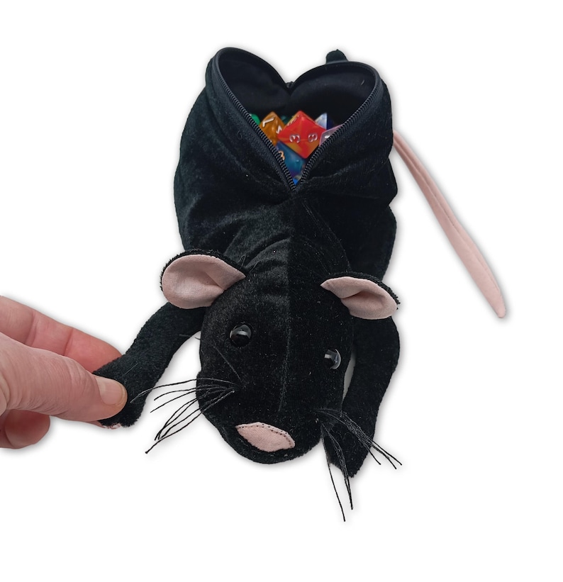 Pu&ograve; includere: Sacchetto da gioco in peluche nero a forma di topo con coda e orecchie rosa. Il sacchetto &egrave; aperto e pieno di dadi colorati.