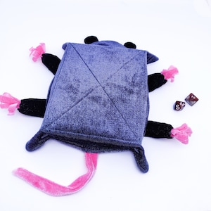 May include: A plush grey rat toy with pink ears and tail. The rat is lying on its back with its legs and tail spread out. Two red dice are visible in the background.