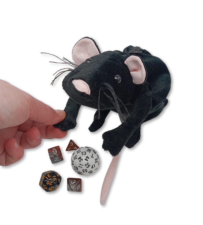 Pu&ograve; includere: Sacchetto da dado in peluche nero a forma di topo con naso e orecchie rosa. Il sacchetto &egrave; aperto e una mano ci sta entrando. Ci sono quattro dadi sul tavolo accanto al sacchetto, tra cui un d20, un d6, un d4 e un d100.