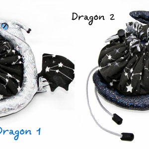 Op de afbeelding: Twee zwarte en witte dobbelstenen zakken in de vorm van draken. De draak links is zilver en de draak rechts is blauw. Beide draken hebben een sterrenbeeldpatroon op hun vleugels. De dobbelstenen zak rechts heeft een witte dobbelsteen ernaast.