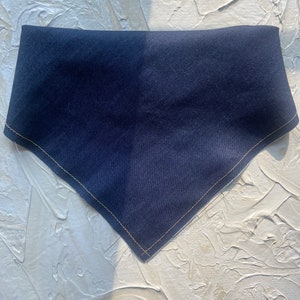 May include: A navy blue bandana with a triangular shape. The edges are finished with a light tan stitching. The bandana is made of a soft fabric and is suitable for pets.