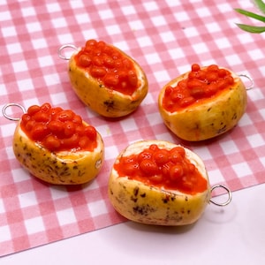 Puede incluir: Cuatro amuletos de patata al horno con frijoles rojos en la parte superior. Cada amuleto tiene un lazo plateado para colgar.