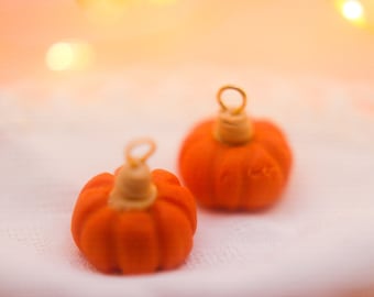 May include: Two small orange pumpkin-shaped ornaments with gold wire loops. The ornaments are on a white surface.