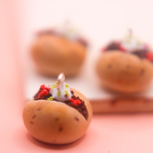 May include: Three miniature food charm pendants, each shaped like a small bun with a white frosting topping and red and green sprinkles. The charms are made of polymer clay and are designed to look like miniature food.