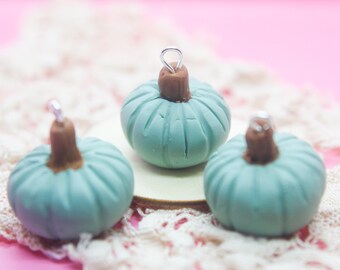 May include: Three small teal blue ceramic pumpkins with brown stems and silver wire loops. The pumpkins are sitting on a white lace doily.