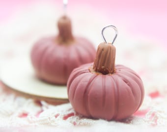 May include: Two small, red clay pumpkins with wire loops for hanging. The pumpkins are on a white lace surface.
