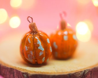 May include: Two small orange and white pumpkin-shaped ornaments with a wire loop on top. The ornaments are sitting on a wooden slice.
