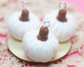 May include: Three white ceramic pumpkins with brown stems and silver wire loops. The pumpkins are sitting on a wooden plate.