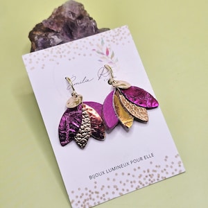 Puede incluir: Pendientes colgantes con diseño floral. Los pendientes presentan elementos metálicos fucsia y dorados en forma de pétalo. Se exhiben en una tarjeta blanca con el texto "BIJOUX LUMINEUX POUR ELLE".