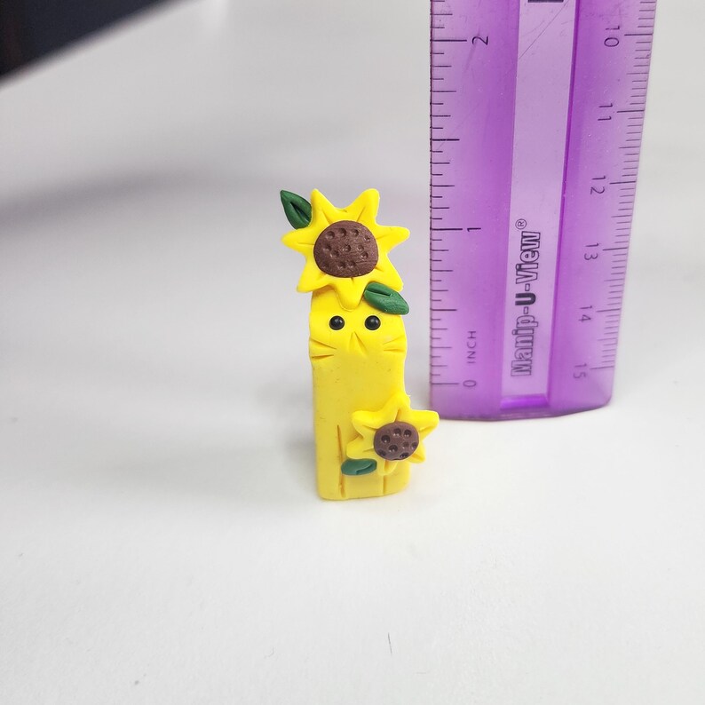 May include: A yellow figurine of a sunflower with a face and two sunflowers on top. The figurine is about 2 inches tall.