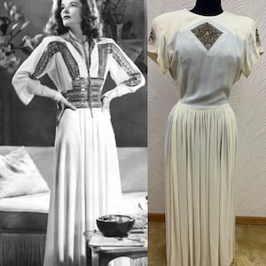 Puede incluir: Un vestido blanco de largo hasta el suelo con un corpiño de cuentas y mangas cortas. El vestido tiene un corpiño ajustado y una falda fluida.