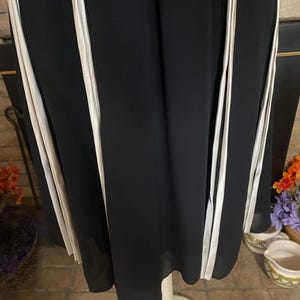 May include: Black dress with vertical white stripes. The dress is displayed on a white mannequin. The fabric appears to be flowing and lightweight. The dress has a simple, elegant design, suitable for various occasions.