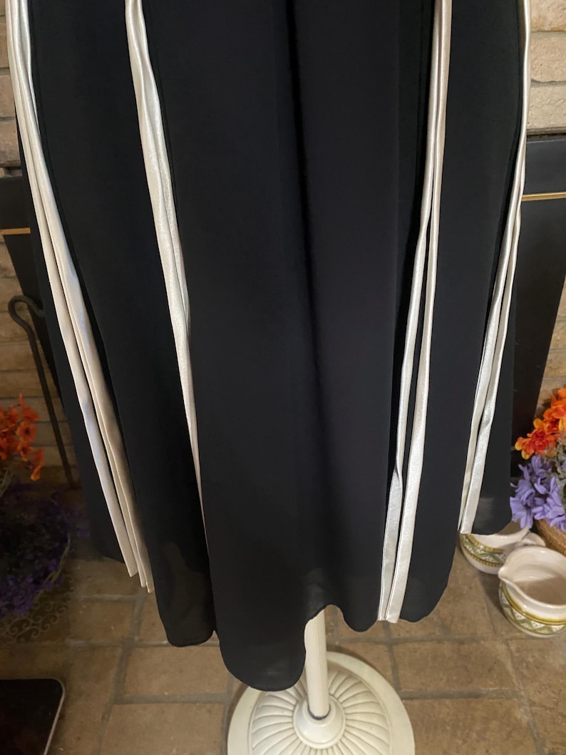 May include: Black dress with vertical white stripes. The dress is displayed on a white mannequin. The fabric appears to be flowing and lightweight. The dress has a simple, elegant design, suitable for various occasions.
