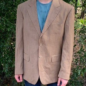 May include: A striped blazer with a brown and beige pattern. The blazer has a single breasted closure with three buttons.