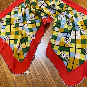 May include: A vintage silk scarf with a vibrant checkered pattern in green, yellow, and blue, featuring repeating cartoon figures. The scarf has a bright red border and a scalloped edge, creating a striking contrast.