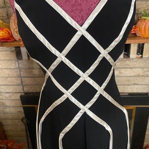 May include: Black sleeveless dress with a white lattice design. The dress has a V-neckline and a fitted silhouette. The white accents create a geometric pattern across the bodice and skirt.