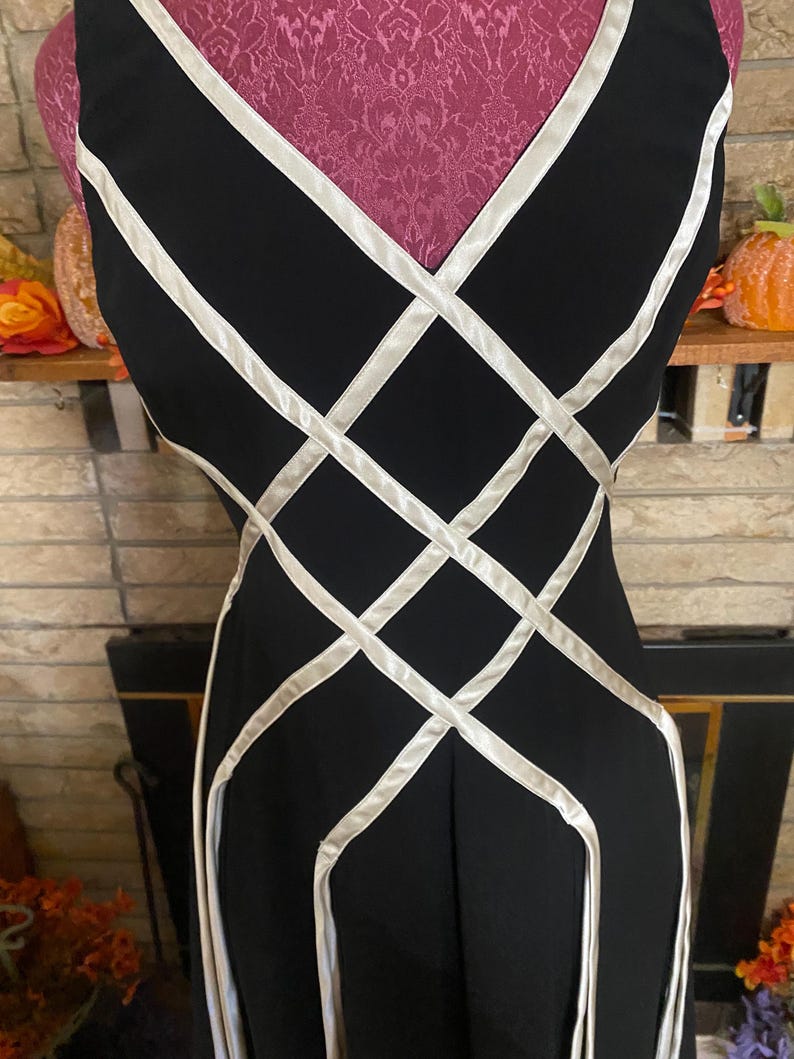 May include: Black sleeveless dress with a white lattice design. The dress has a V-neckline and a fitted silhouette. The white accents create a geometric pattern across the bodice and skirt.
