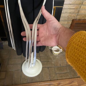 May include: A black dress with white trim and straps. The dress is displayed on a white dress form with a round base. The straps are held by a person's hand.