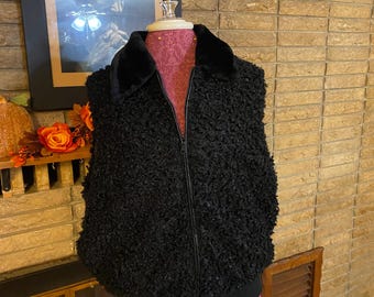 May include: A black textured vest with a black faux fur collar and a full-length zipper. The vest is displayed on a pink dress form. The bottom of the vest has a black band. The vest is a stylish outerwear garment.