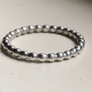 May include: A silver ring with a beaded design. The ring is made of a smooth, shiny metal and has a simple, elegant look.