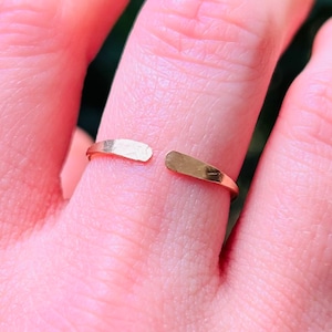 May include: A gold-toned open ring with a hammered finish. The ring is worn on a finger.