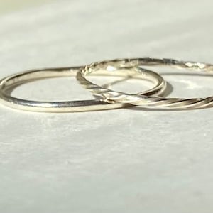 May include: Two silver rings, one plain and one twisted, are stacked on top of each other.
