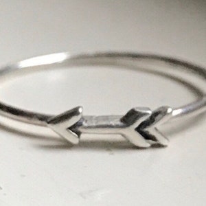 May include: A silver ring with a simple arrow design. The arrow is pointing to the right.