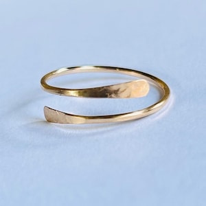 May include: A gold-toned, hammered metal ring with a unique, open design. The ring is made of a single piece of metal that is twisted and wrapped around the finger.