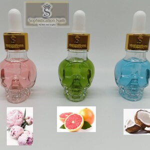 May include: Three glass bottles shaped like skulls filled with colored liquids. The bottles have gold lids and droppers. The bottles are arranged in a row from left to right: pink, green, and blue. Below each bottle is a picture of a flower, fruit, or coconut.